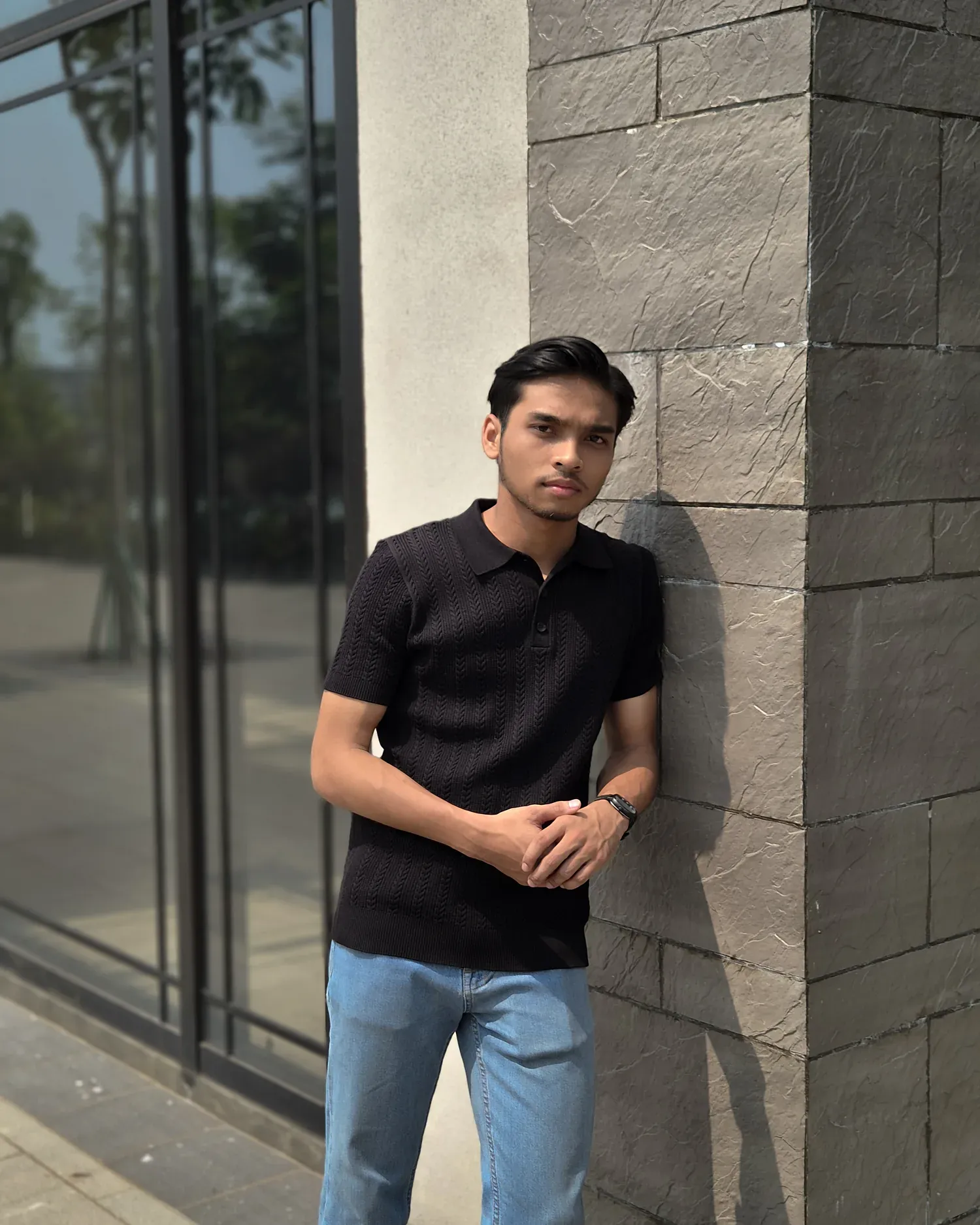Pria mengenakan Mazly Signature Polo hitam di antara fasad bata dan kaca