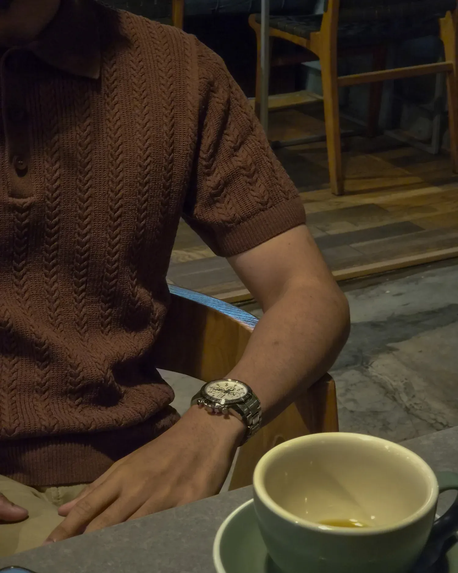Pria duduk di kafe mengenakan Mazly Signature Polo cokelat tua dengan secangkir kopi di meja
