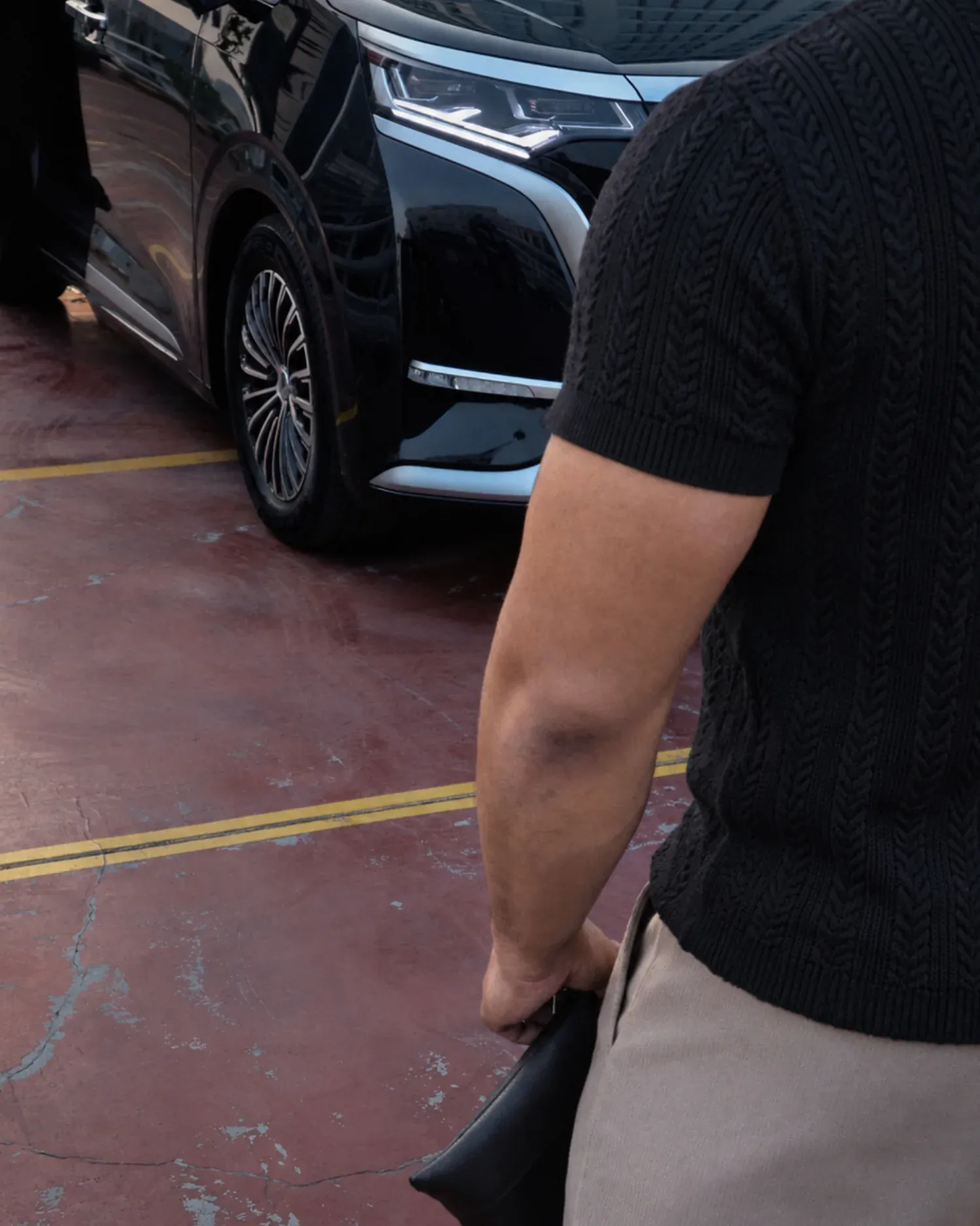 Detail Mazly Signature Polo hitam dari samping dengan mobil di area parkir