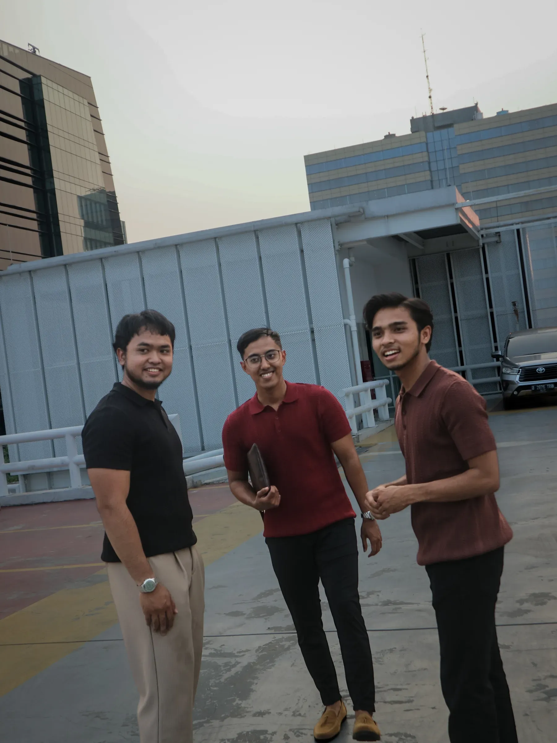 Tiga pria berdiri berbincang mengenakan Mazly Signature Polo hitam, marun muda, dan cokelat tua